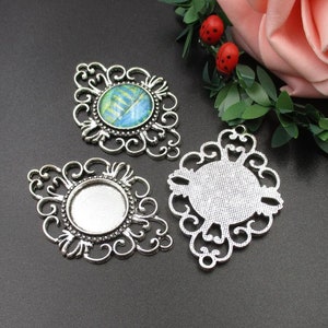May include: Three silver-coloured filigree pendant trays. One tray features a round, colourful abstract design. The other two trays have a blank, round surface for adding your own design. The trays have an ornate, openwork design.
