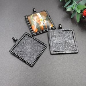 May include: Three black metal square pendant trays with a beaded edge. One tray has a photo of a person inside. The other two trays are empty.