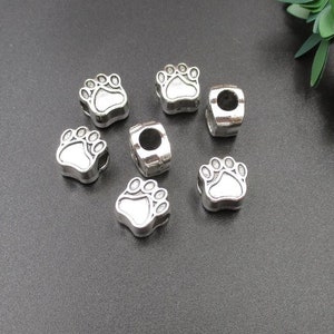 May include: Seven silver charm beads with a paw print design. The beads are small and have a hole in the center for threading onto a bracelet or necklace.