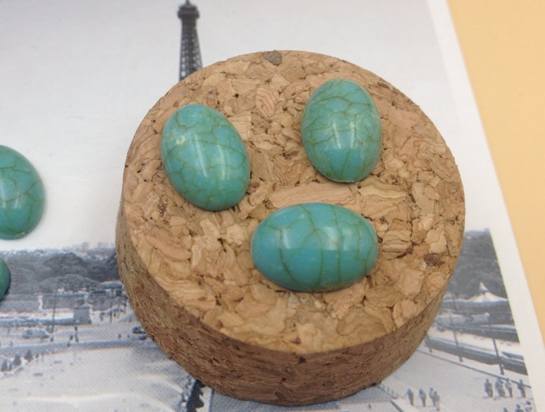 May include: Three turquoise oval cabochons with a marbled pattern, displayed on a cork surface.