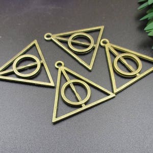 May include: Five gold-toned metal charms shaped like triangles with a circle inside. Each charm has a loop at the top for attaching to a necklace or bracelet.