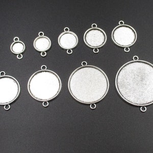Puede incluir: Surtido de bandejas redondas para colgantes de metal plateado con un acabado liso y brillante. Las bandejas tienen dos bucles en la parte superior y son de varios tamaños.