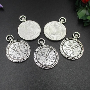 Op de afbeelding: Vijf zilverkleurige zakhorlogebedels met Romeinse cijferklokken. De bedels hebben een gedetailleerd ontwerp en een lus aan de bovenkant om aan sieraden of knutselwerk te bevestigen. De achterkanten van de bedels hebben een zonnestraalpatroon.