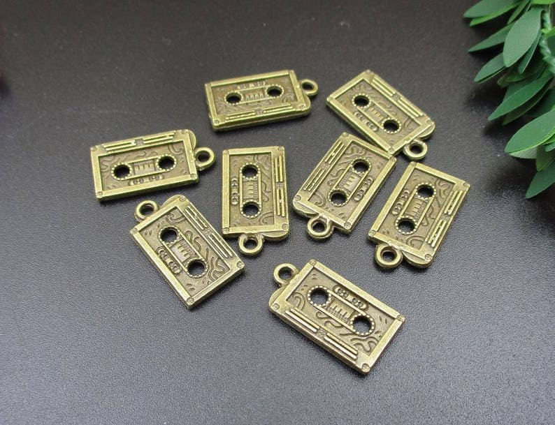 Puede incluir: Una colecci&oacute;n de ocho abalorios de metal dorado antiguo con forma de cintas de casete. Los abalorios tienen un aspecto vintage y son perfectos para a&ntilde;adir un toque de nostalgia a las joyas o las manualidades.