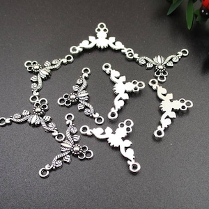 Könnte beinhalten: Ein Satz von acht silberfarbenen Metall-Anhängern mit floralen Designs. Die Anhänger sind V-förmig und haben drei Ösen zum Anbringen an Schmuck oder andere Bastelarbeiten.