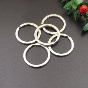 May include: Five silver key rings, all linked together. The rings are round and smooth, with a polished finish.
