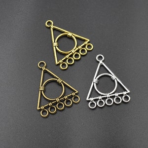 May include: Three triangle-shaped metal charms with a circle in the center and five small circles hanging from the bottom. The charms are in gold and silver.