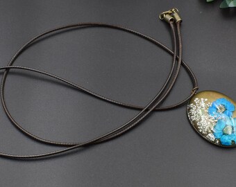 May include: A brown leather cord necklace with a silver oval pendant featuring a pressed blue flower design.