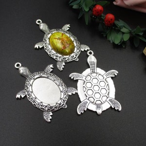 Puede incluir: Tres dijes de tortuga plateada con un marco de camafeo. Una tortuga tiene un camafeo verde y amarillo, mientras que las otras dos tienen marcos de camafeo en blanco.
