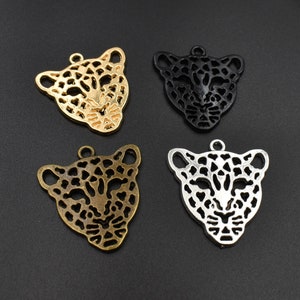Puede incluir: Cuatro abalorios de metal con forma de cabeza de leopardo en oro, plata y negro. Los abalorios están detallados con un patrón de manchas y tienen un bucle en la parte superior para sujetarlos a joyas.