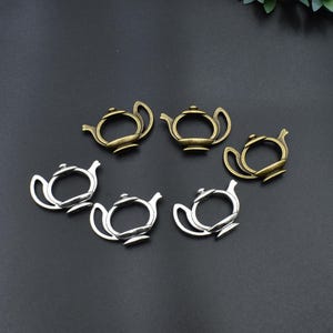 Könnte beinhalten: Sechs Teekannen-Anhänger aus Metall in Antikgold- und Silberfarben sind auf einer dunklen Oberfläche angeordnet. Die Anhänger sind mit Griffen, Ausgüssen und Deckeln versehen, ideal für Schmuckherstellung oder Bastelprojekte.