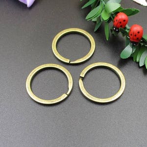 May include: Three gold-toned metal key rings, each with a circular shape. The key rings are arranged in a triangular pattern on a dark gray surface.