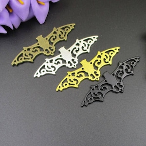 May include: Four metal bat cutouts in different colours: gold, silver, black, and gold. The cutouts are intricate and detailed, with a delicate design.