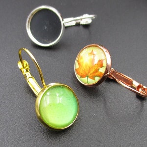 May include: Three pairs of earrings with different colored glass cabochons. The first pair has a clear glass cabochon, the second pair has a green glass cabochon, and the third pair has a brown glass cabochon with a pressed leaf design.