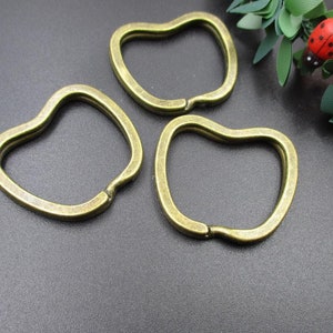 May include: Three gold-toned metal keychains shaped like apples. The keychains are on a dark gray surface.