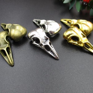 May include: Three bird skull charms in silver, gold, and bronze finishes. The charms are detailed with intricate bone and beak features.