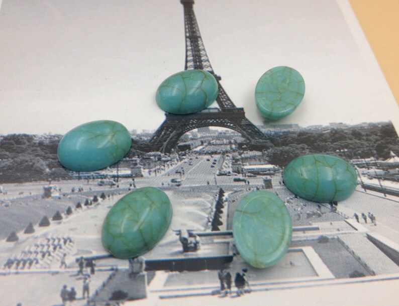 May include: Six oval-shaped turquoise cabochons with a marbled pattern. The cabochons are arranged in a semi-circle on a white background with a black and white image of the Eiffel Tower in the background.
