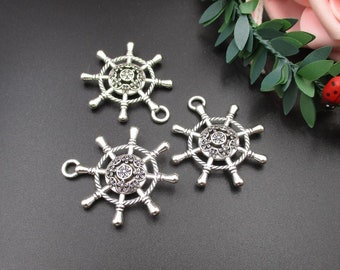 May include: Three silver-toned metal ship wheel charms with intricate details. Each charm has a circular design with spokes radiating outwards and a smaller circular design in the center.