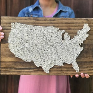May include: A wooden sign with a white string art design of the United States of America.
