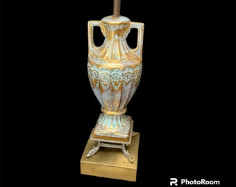 May include: A gold and white ceramic table lamp with an urn-shaped base and a gold metal base. The lamp has a white and gold design with a distressed finish.