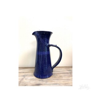 May include: A dark blue ceramic pitcher with a wide mouth and a handle. The pitcher has a speckled glaze.