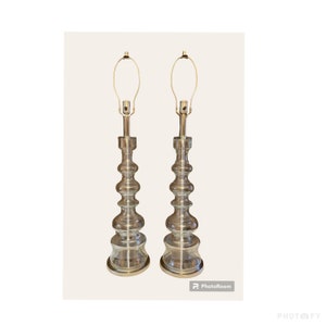 May include: A pair of clear glass table lamps with gold metal bases. The lamps have a unique, layered design with a bulbous shape.