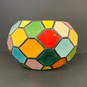 May include: A multi-colored ceramic planter shaped like a soccer ball. The planter is made of individual hexagonal tiles in shades of yellow, red, green, blue, and pink.