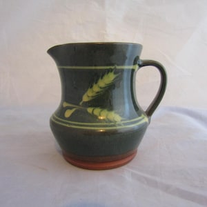 May include: A green ceramic pitcher with a brown rim and a yellow wheat design.