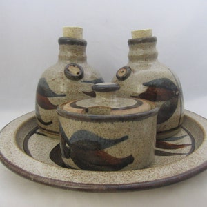 May include: A ceramic serving set with a tray, two bottles, and a lidded jar. The set is decorated with a brown, black, and white floral pattern.
