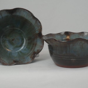 May include: Two ceramic bowls with a scalloped, wavy rim design. The bowls feature a deep blue and brown glaze with a glossy finish, showing vertical drip patterns. The interior and exterior surfaces display a blend of dark tones and blue hues.