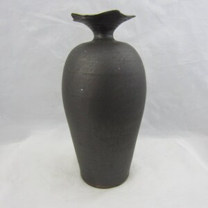 May include: A dark gray ceramic vase with a unique, asymmetrical opening at the top.