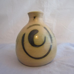Peut inclure: Un petit vase en céramique de couleur crème avec un motif abstrait bleu foncé et vert. Le vase a un corps arrondi et un col étroit.