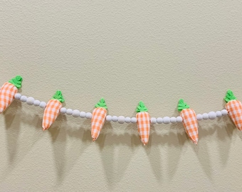 May include: A garland of orange and white gingham carrots with green tops strung on a white beaded string.