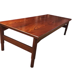 Peut inclure: Une table basse en bois brun foncé avec un plateau rectangulaire et un design simple et moderne. La table a une seule poutre de soutien horizontale et quatre pieds.