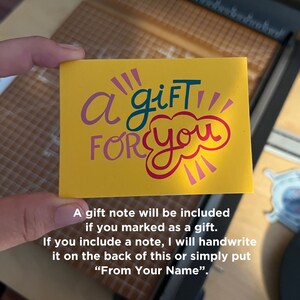 May include: A yellow gift note with the words "a gift FOR you" in a playful font. The note includes text about handwritten messages and gift options. The note is held in a person's hand.