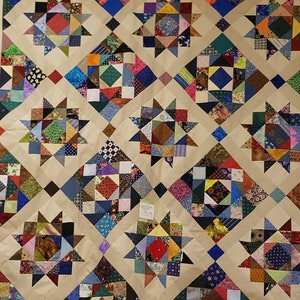 May include: A beige quilt with a patchwork design featuring a repeating pattern of stars made from colorful fabric squares. The quilt is hanging on a wall with a sign that reads "Learn to Use Cricut Explore".