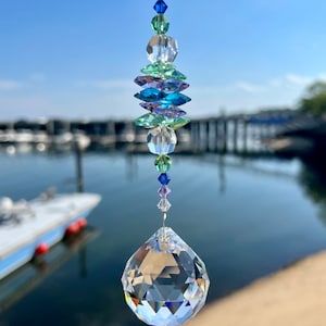 May include: A crystal suncatcher with a large clear crystal teardrop at the bottom and a multi-colored crystal strand above. The strand features blue, green, and purple crystals.