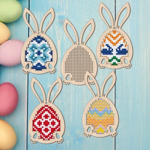 May include: Five wooden bunny-shaped ornaments with a hole for hanging. Each bunny holds a different coloured Easter egg with a geometric pattern. The eggs are blue, orange, red, yellow, and pink.