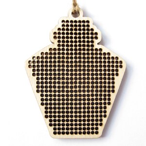 May include: A wooden ornament shaped like a house with a grid pattern for cross-stitch embroidery.