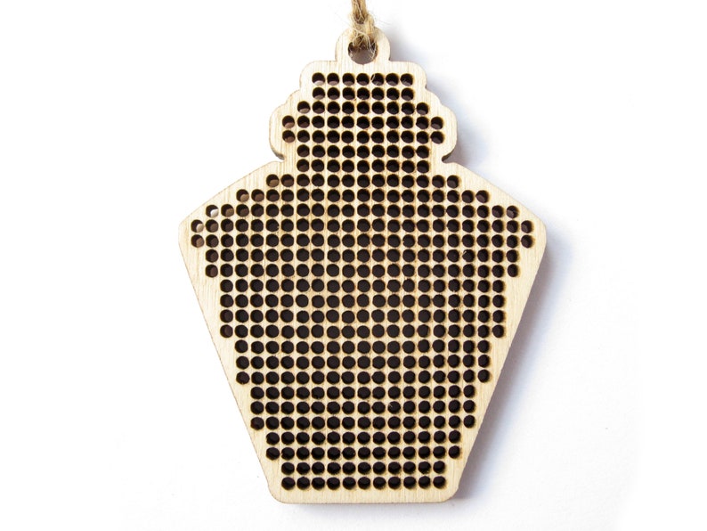 May include: A wooden ornament shaped like a house with a grid pattern for cross-stitch embroidery.