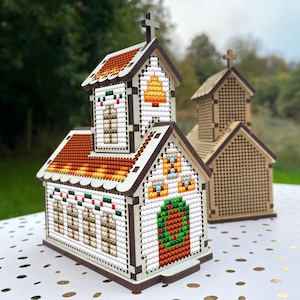 May include: Two wooden Christmas church buildings with cross accents and detailed cross-stitch designs. The larger church has a wreath on the door and a small tree on the roof. The smaller church is plain.