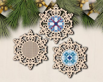May include: Three wooden snowflake ornaments with intricate designs. Two of the snowflakes have blue and white cross-stitch patterns in the center, while the third snowflake has a blank center.