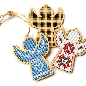 May include: Three wooden angel ornaments with cross-stitch designs. One angel features a blue and white pattern, another has a red and green design, and the third is unfinished. Each has a jute string for hanging.