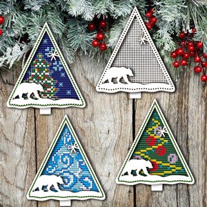 Può includere: Quattro decorazioni per l'albero di Natale in legno con un design di orso bianco e diversi disegni ricamati colorati. Le decorazioni sono appese su uno sfondo di legno.
