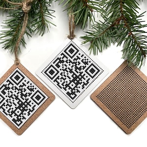 May include: Three wooden ornaments with different designs. One ornament features a black and white QR code, another has a black and white pixelated design, and the third has a black and white dot pattern.