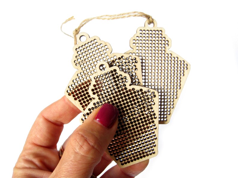 May include: Three unfinished wooden ornaments shaped like bottles with a grid pattern for cross-stitch embroidery.