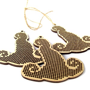May include: Three unfinished wooden ornaments shaped like a cloud with a swirl design. The ornaments are made of light brown wood and have a textured surface. They are strung together with twine.