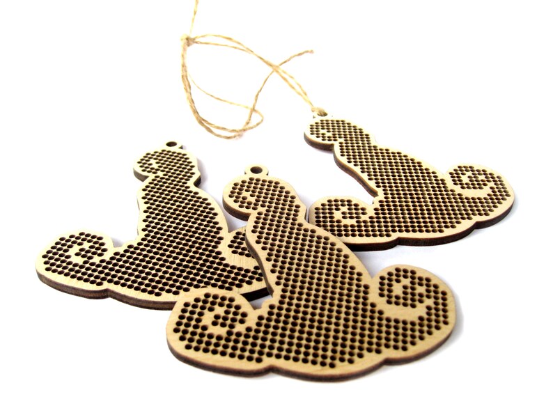May include: Three unfinished wooden ornaments shaped like a cloud with a swirl design. The ornaments are made of light brown wood and have a textured surface. They are strung together with twine.