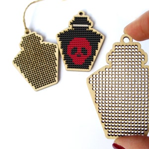 May include: Three wooden ornaments with a grid pattern for cross-stitch. One ornament is blank, one has a black and red skull design, and one has a black and white design.