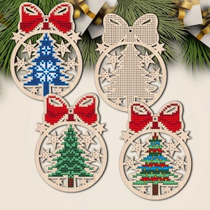 Peut inclure: Quatre ornements de Noël en bois avec un design festif. Chaque ornement présente un nœud rouge, un cadre circulaire avec des découpes d'étoiles et un sapin de Noël au point de croix de différentes couleurs, dont le bleu, le vert et le rouge. Les ornements sont présentés sur un fond de branches de pin.